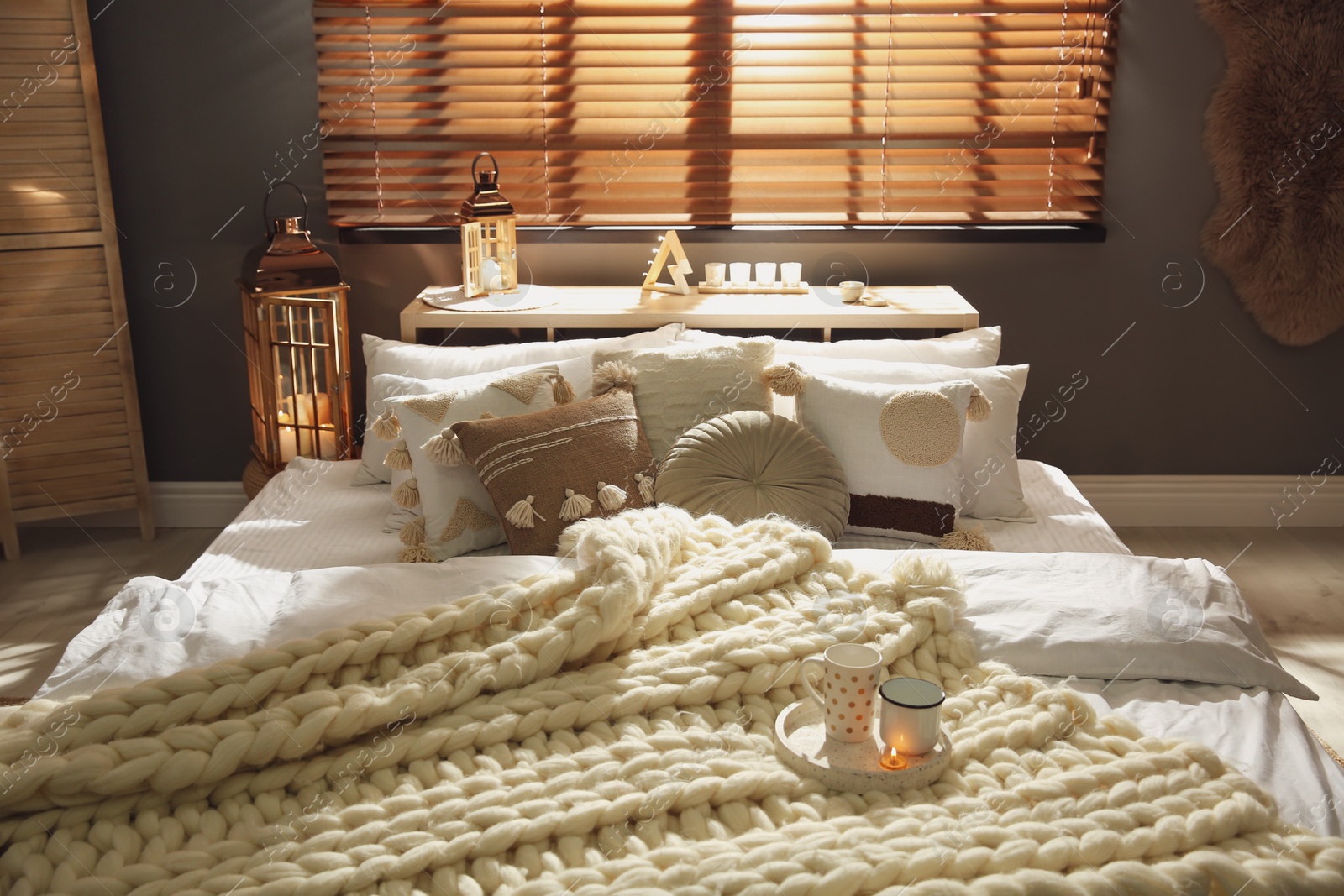 Photo of Bed with cozy knitted blanket and cushions near window in room. Interior design