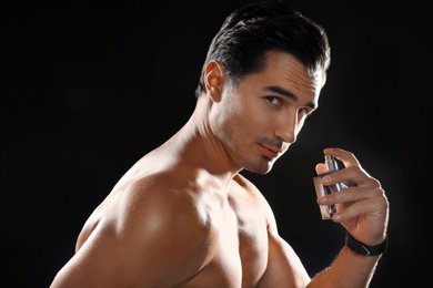 Handsome young man using perfume on black background