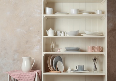 Photo of Stylish storage stand with different ceramic dishware at home