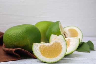 Whole and cut sweetie fruits on white wooden table, closeup