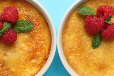 Delicious creme brulee with fresh raspberries in ramekins on light blue background, flat lay