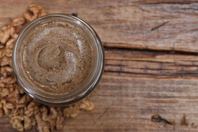 Tasty walnut nut paste in jar on wooden table, top view. Space for text