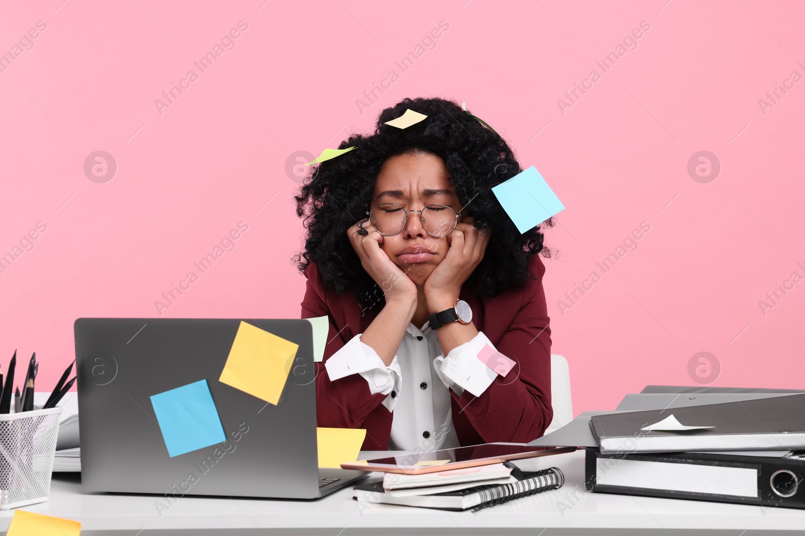 Photo of Stressful deadline. Exhausted woman sitting at white desk against pink background. Sticky notes everywhere as reminders