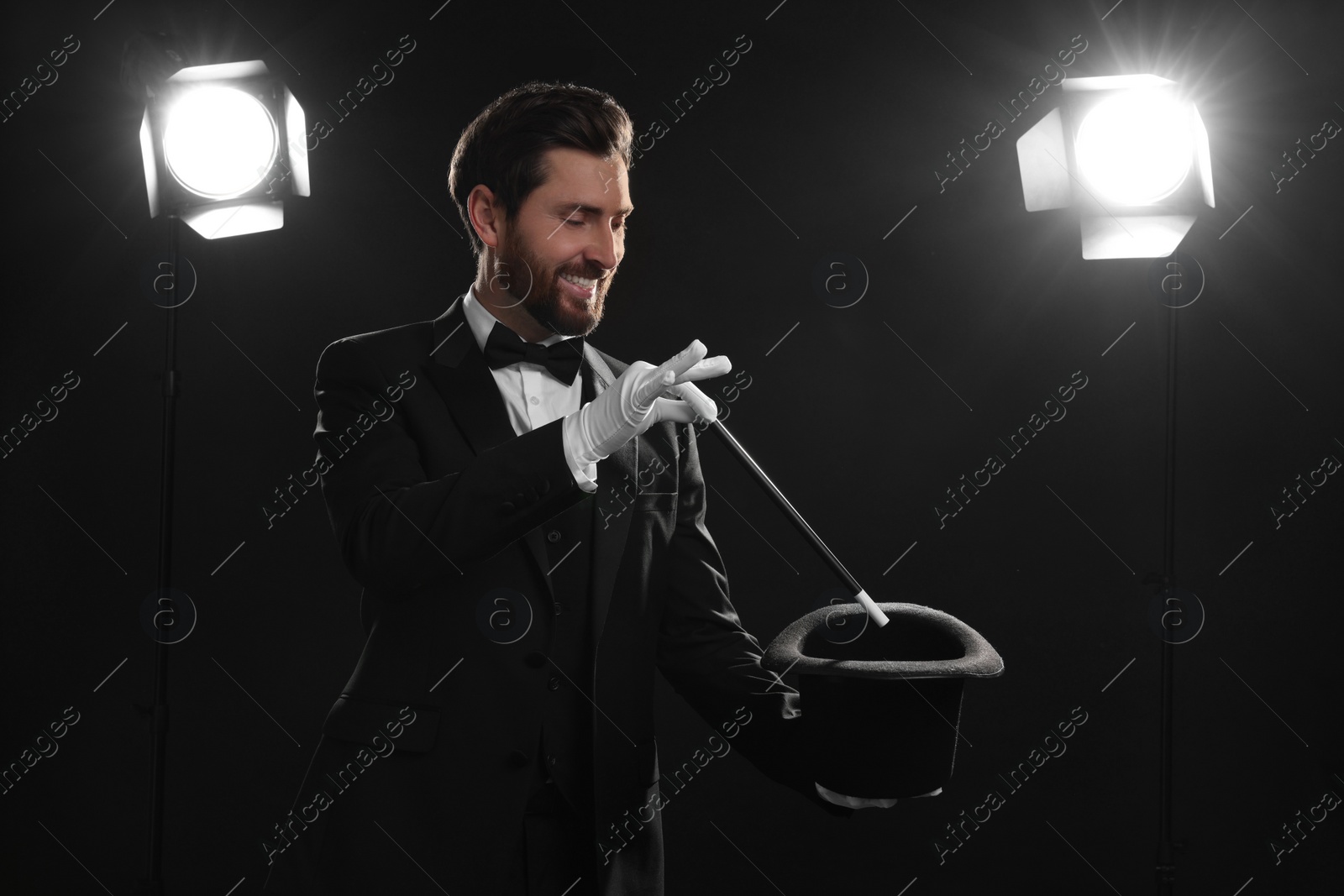 Photo of Happy magician showing magic trick with top hat on stage