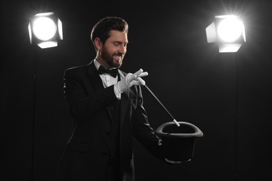 Happy magician showing magic trick with top hat on stage