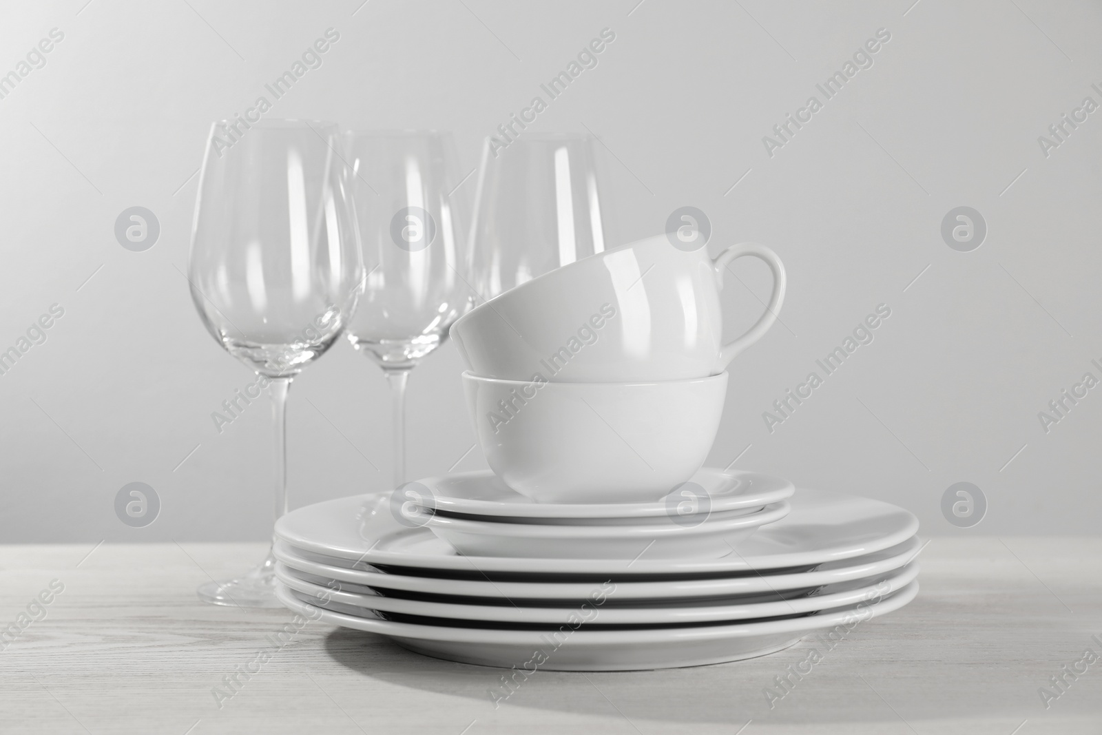 Photo of Set of clean dishware and glasses on white wooden table against light background