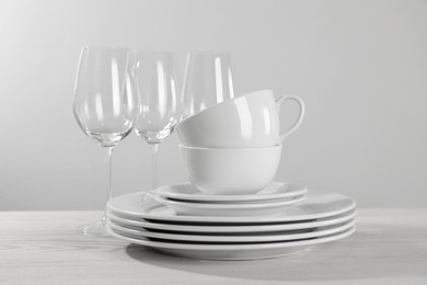 Photo of Set of clean dishware and glasses on white wooden table against light background