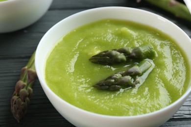 Delicious asparagus soup in bowl on grey wooden table, closeup