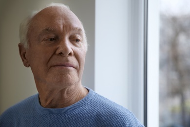 Portrait of elderly man near window indoors. Space for text