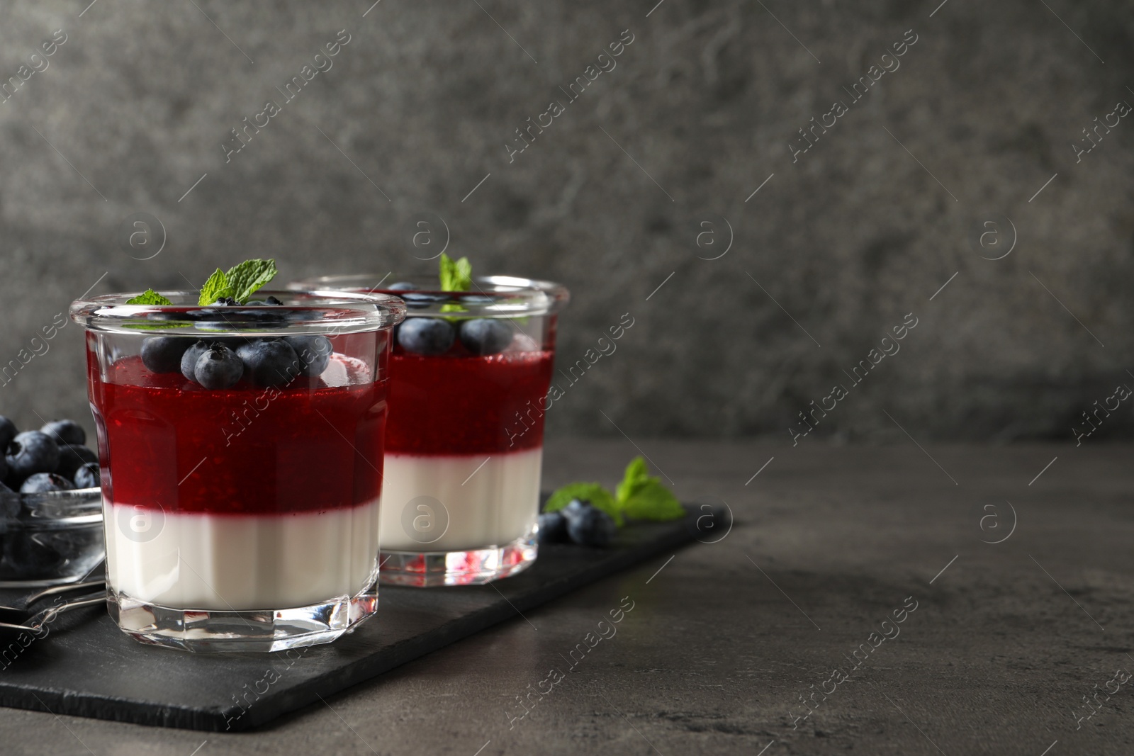 Photo of Delicious panna cotta with fruit coulis and fresh blueberries served on grey table. Space for text