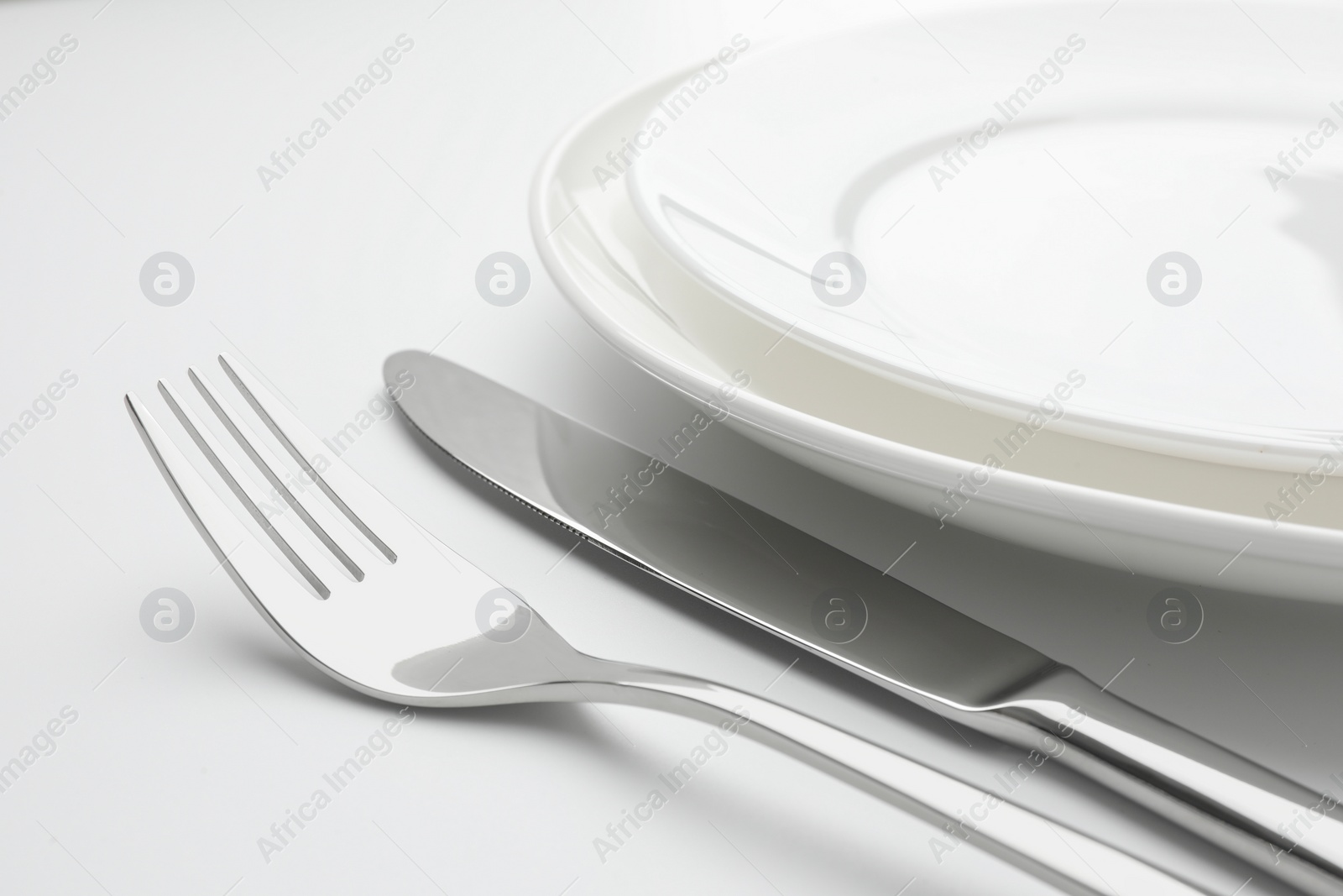 Photo of Clean plates, fork and knife on white background, closeup