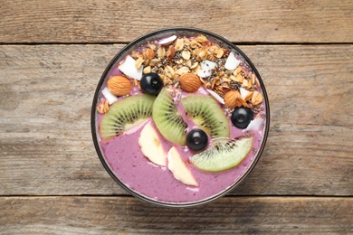 Delicious acai smoothie with granola and fruits in dessert bowl on wooden table, top view