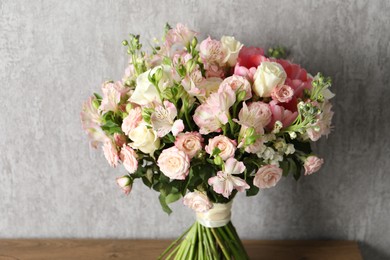 Beautiful bouquet of fresh flowers on wooden table near grey wall