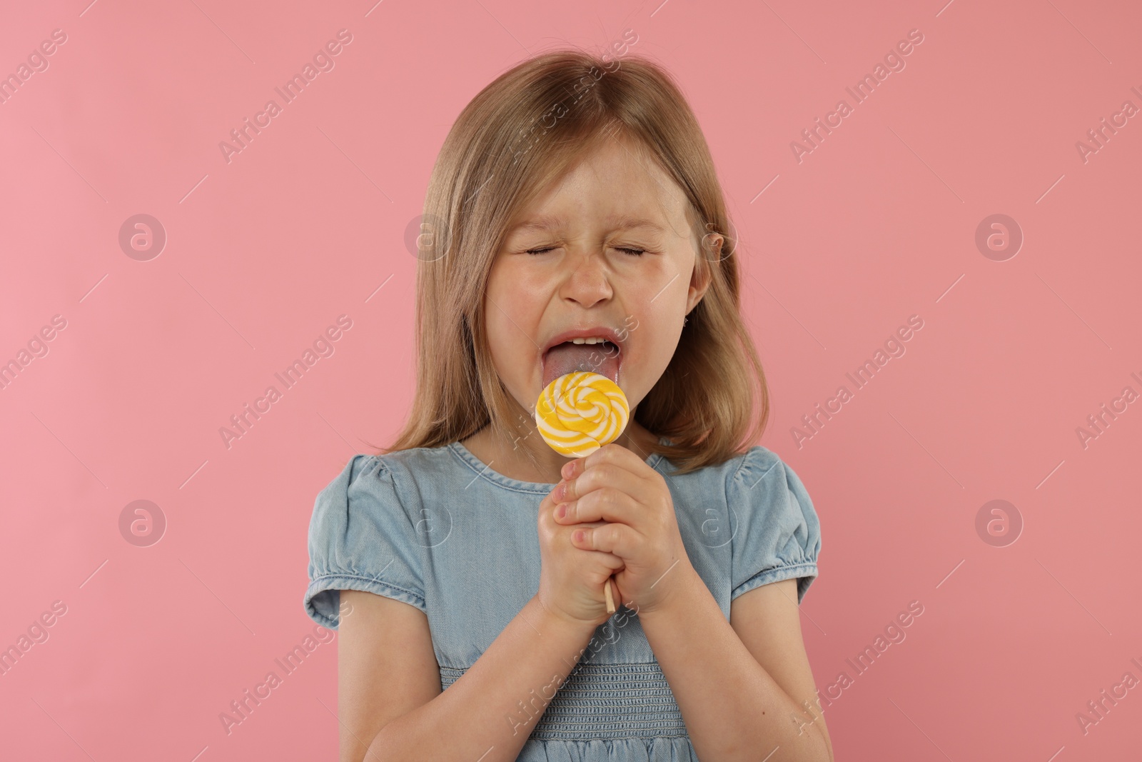 Photo of Cute girl licking lollipop on pink background