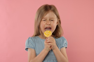 Photo of Cute girl licking lollipop on pink background