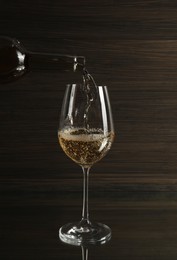 Photo of Pouring white wine from bottle into glass on table against wooden background