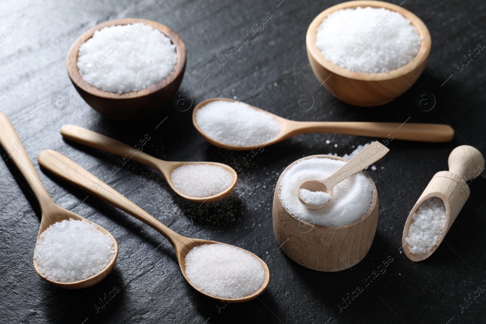 Photo of Organic white salt in bowls and spoons on black table