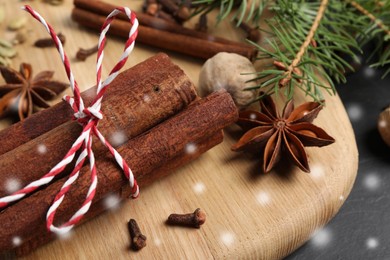 Different spices and fir tree branches on black table, closeup. Cinnamon, cloves, anise, cardamom, nutmeg