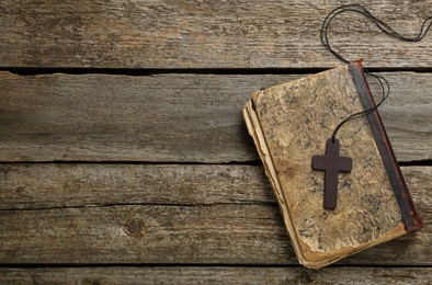 Wooden Christian cross and old Bible on table, top view. Space for text