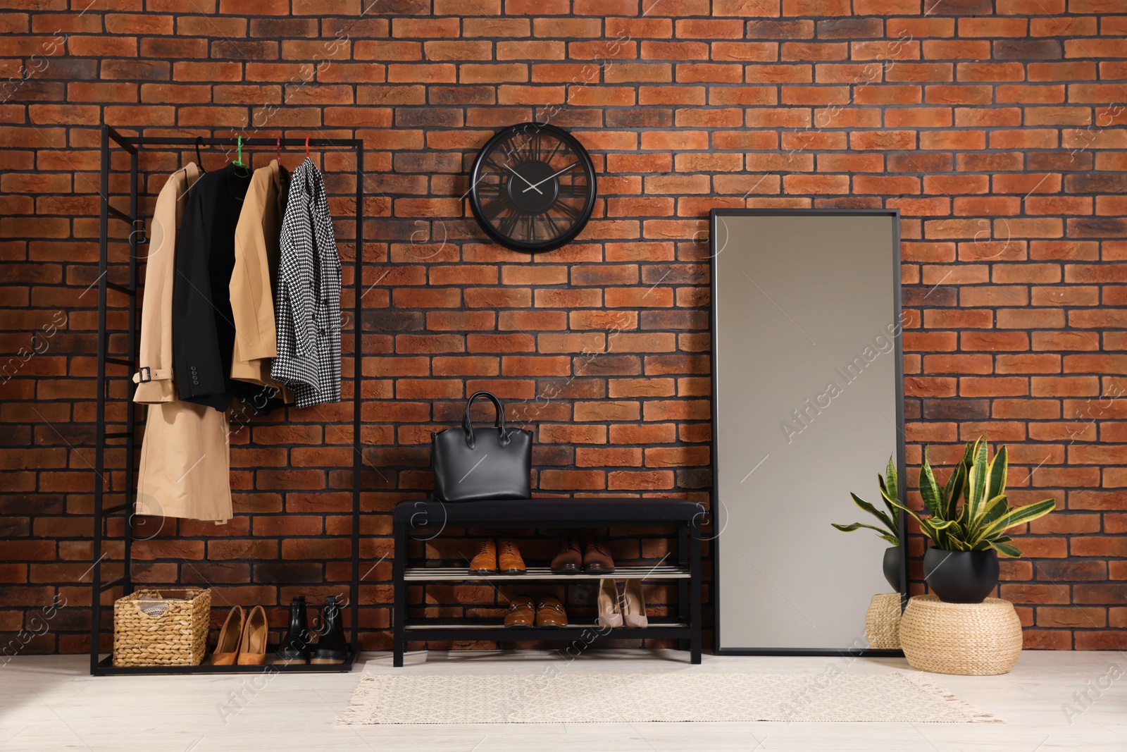 Photo of Stylish hallway with coat rack, mirror and shoe storage bench near brick wall. Interior design