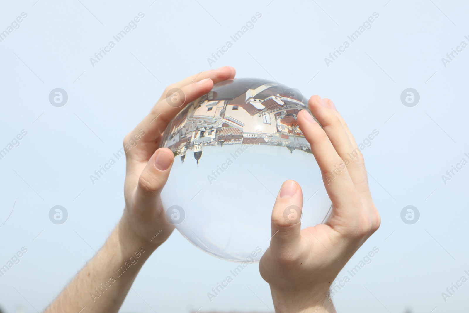 Photo of View of beautiful city street, overturned reflection. Man holding crystal ball against sky, closeup