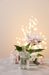 Photo of Bottle of perfume and beautiful lily flowers on table against beige background with blurred lights, space for text