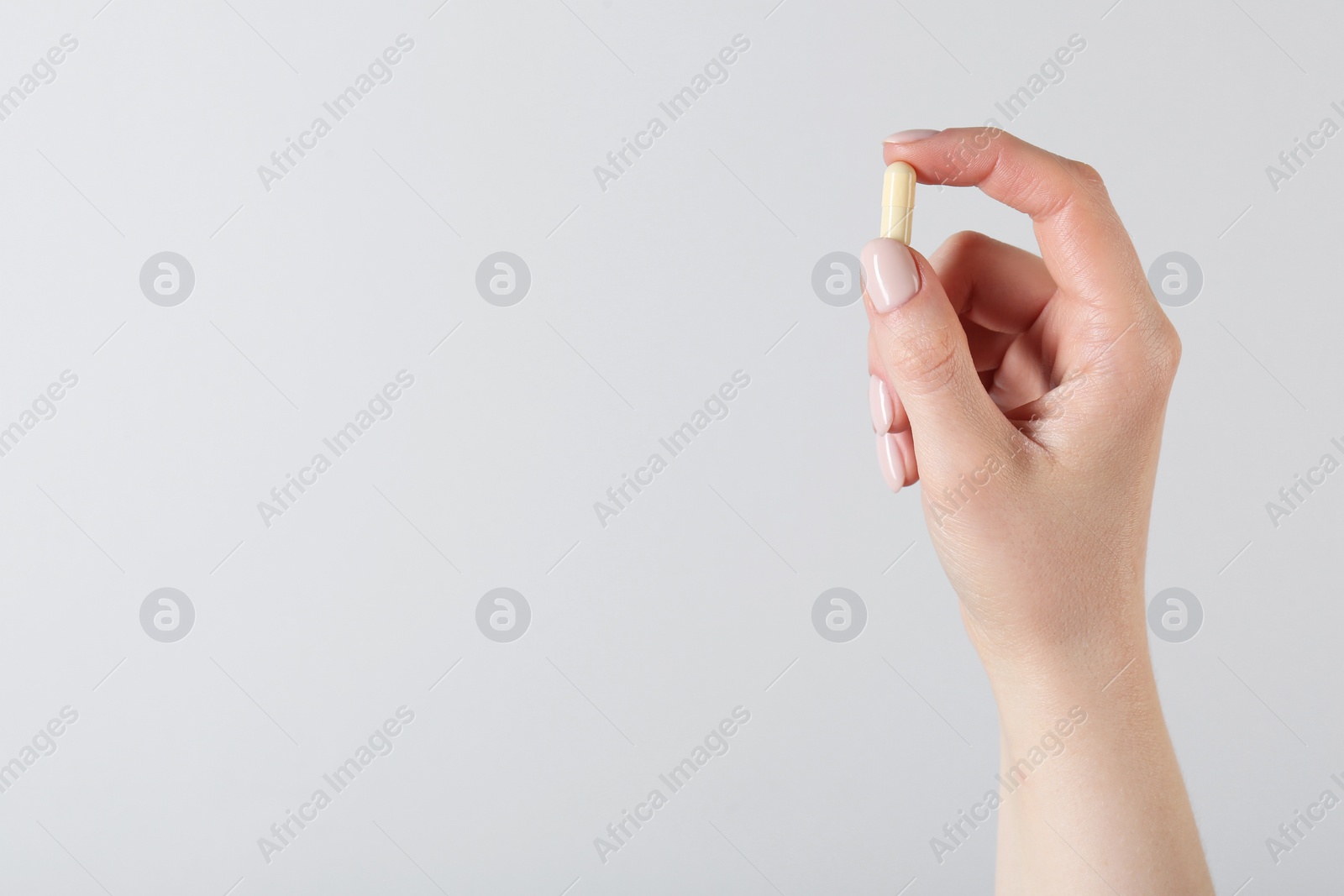 Photo of Woman holding vitamin capsule on light grey background, closeup with space for text. Health supplement