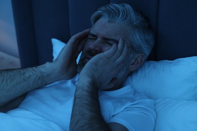 Mature man suffering from headache in bed at night