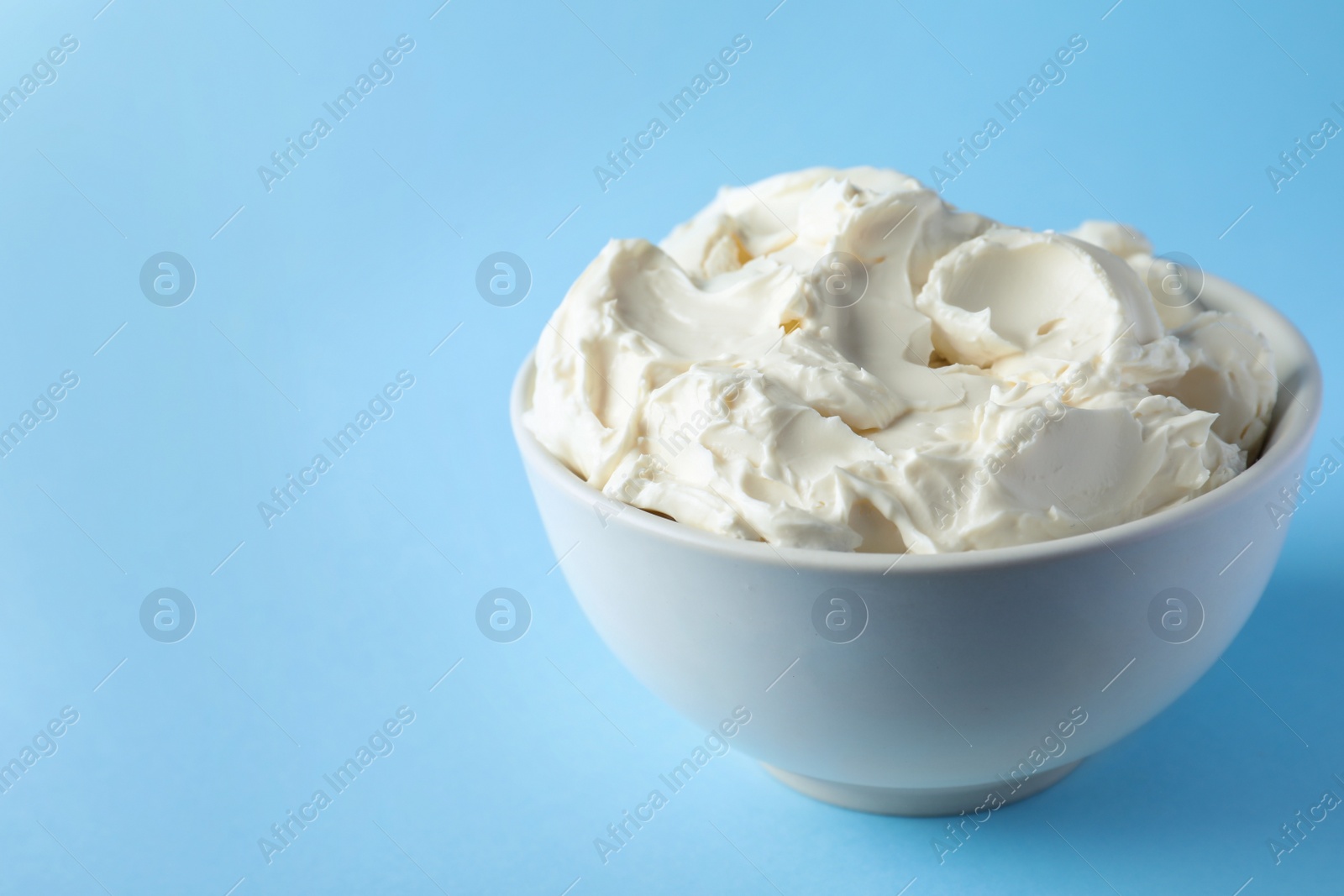 Photo of Bowl of tasty cream cheese on light blue background, space for text