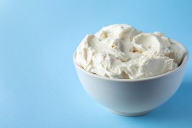 Photo of Bowl of tasty cream cheese on light blue background, space for text