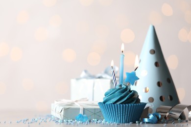 Delicious birthday cupcake with cream and burning candles on white table. Space for text