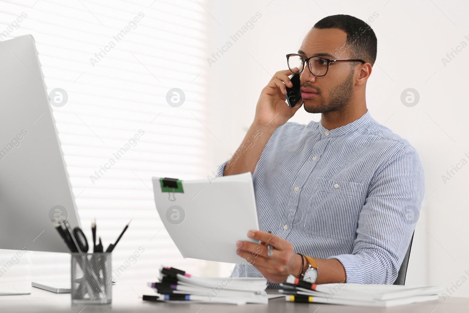 Photo of Man talking on phone while working with documents at wooden table in office