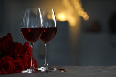 Photo of Glasses of red wine and rose flowers on grey table against blurred lights, space for text. Romantic atmosphere