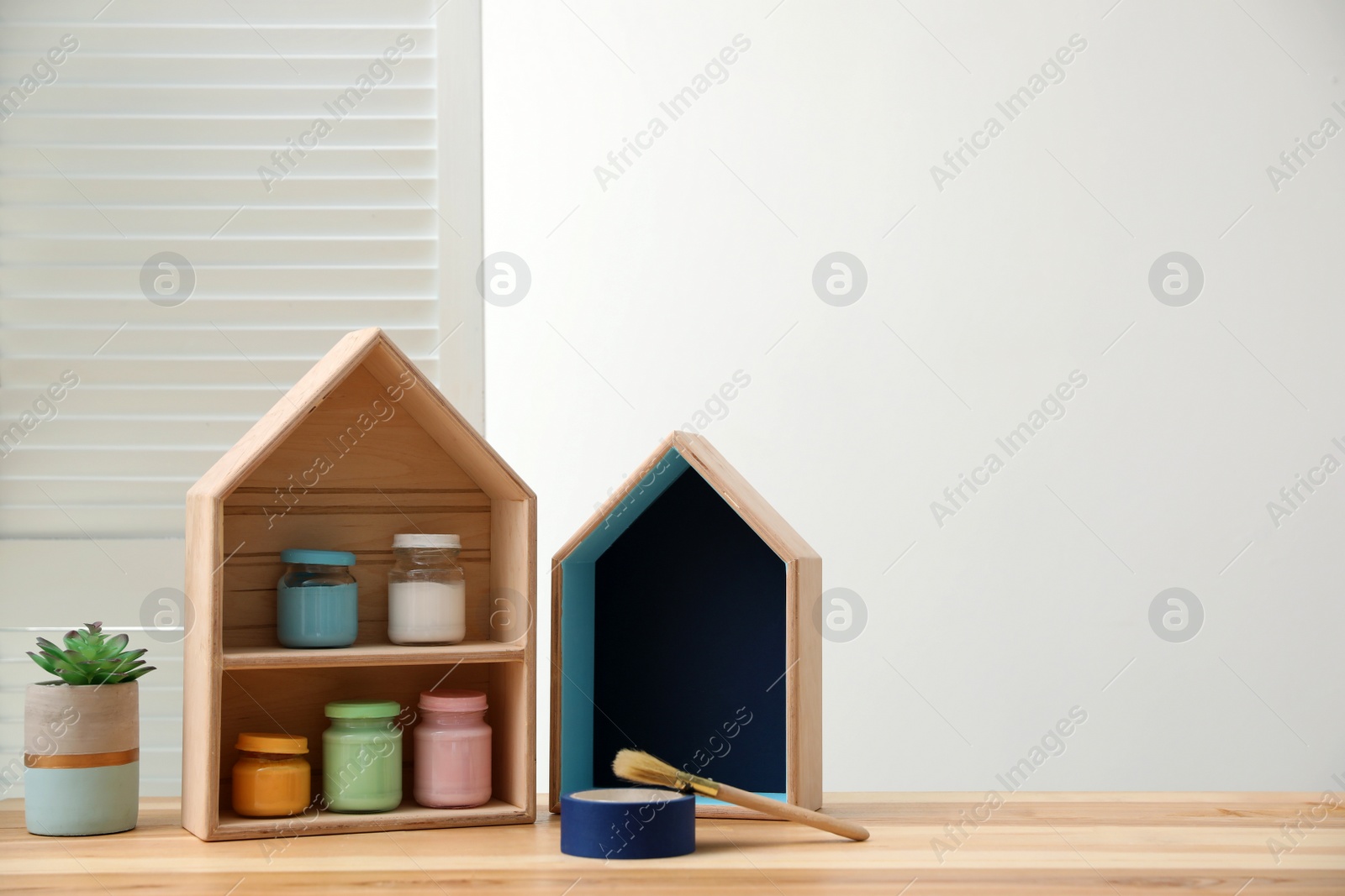 Photo of House shaped shelf brush and jars of paints on table. Space for text