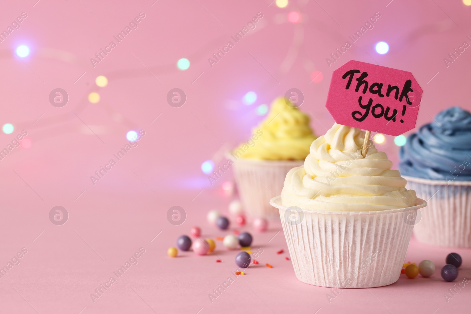 Photo of Tasty cupcakes and note with phrase Thank You on pale pink background, space for text