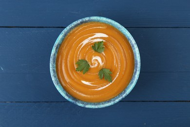 Photo of Delicious pumpkin soup in bowl on blue wooden table, top view
