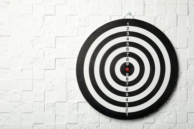 Photo of Dart board hanging on white textured wall. Space for text