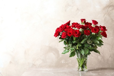 Vase with beautiful red roses on table against color background