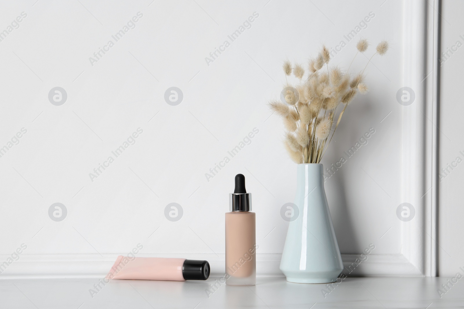 Photo of Skin foundation and dried reeds near white wall, space for text. Makeup product