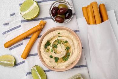 Delicious hummus with grissini sticks, lime and olives on light grey table, flat lay