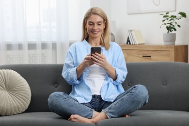 Happy woman sending message via smartphone on couch at home