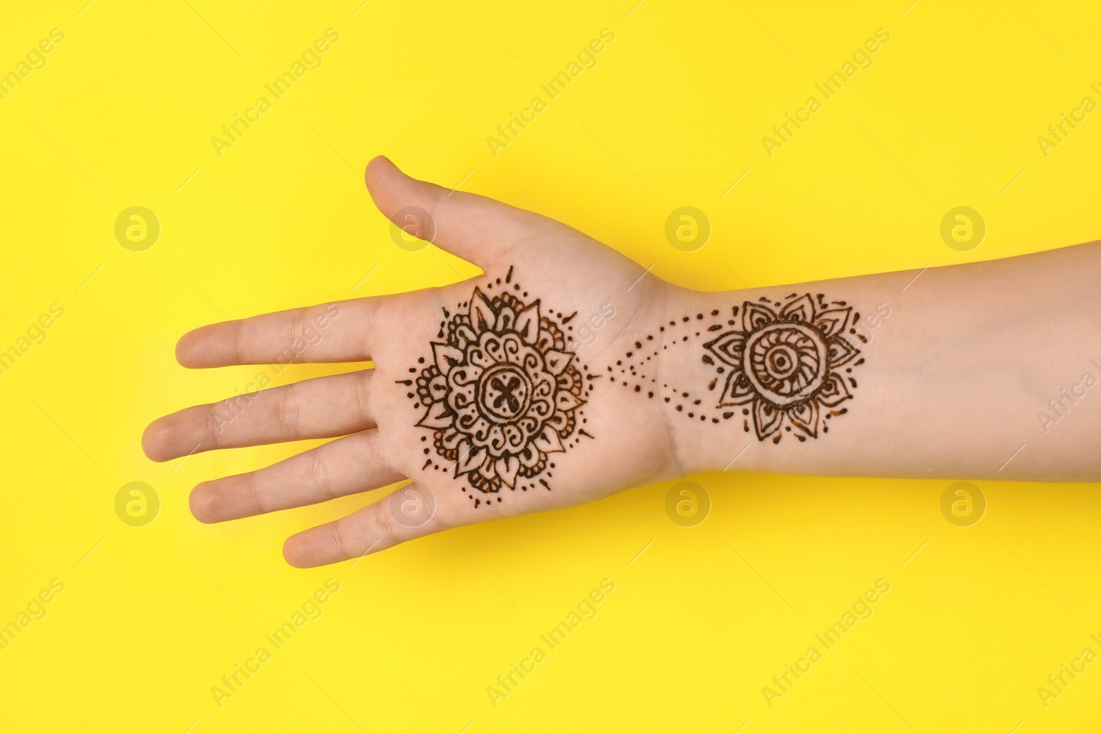 Photo of Little girl with henna tattoo on palm against yellow background, closeup. Traditional mehndi ornament
