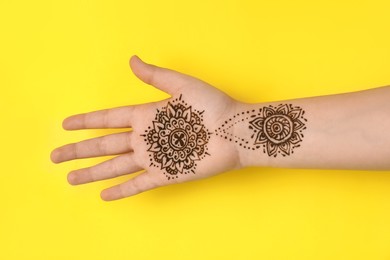 Photo of Little girl with henna tattoo on palm against yellow background, closeup. Traditional mehndi ornament
