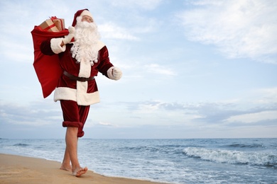 Santa Claus with bag of presents on beach, space for text. Christmas vacation