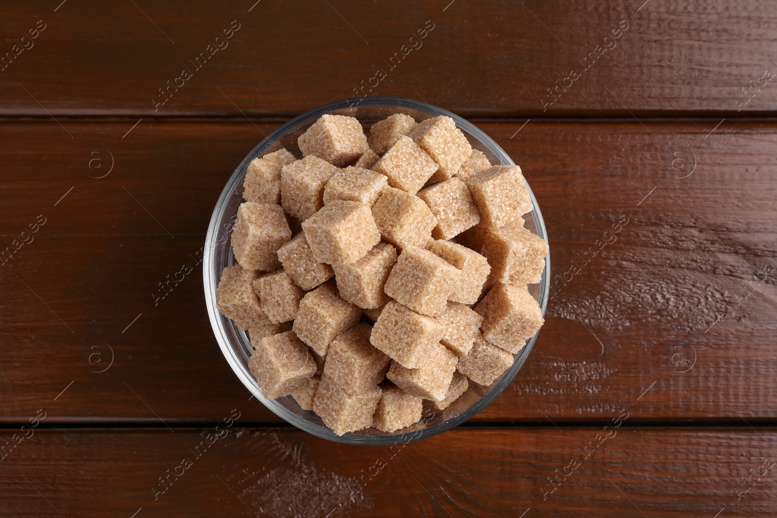 Photo of Brown sugar cubes in glass bowl on wooden table, top view