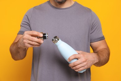 Man opening thermo bottle on orange background, closeup