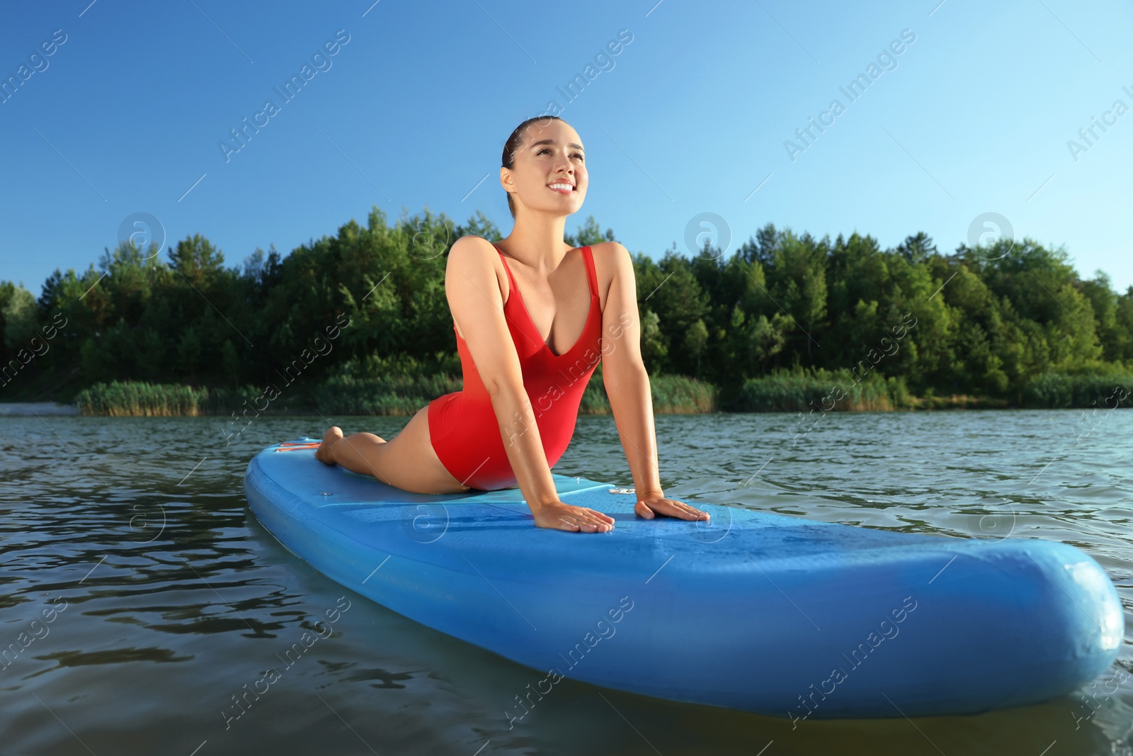 Photo of Young woman practicing yoga on light blue SUP board on river