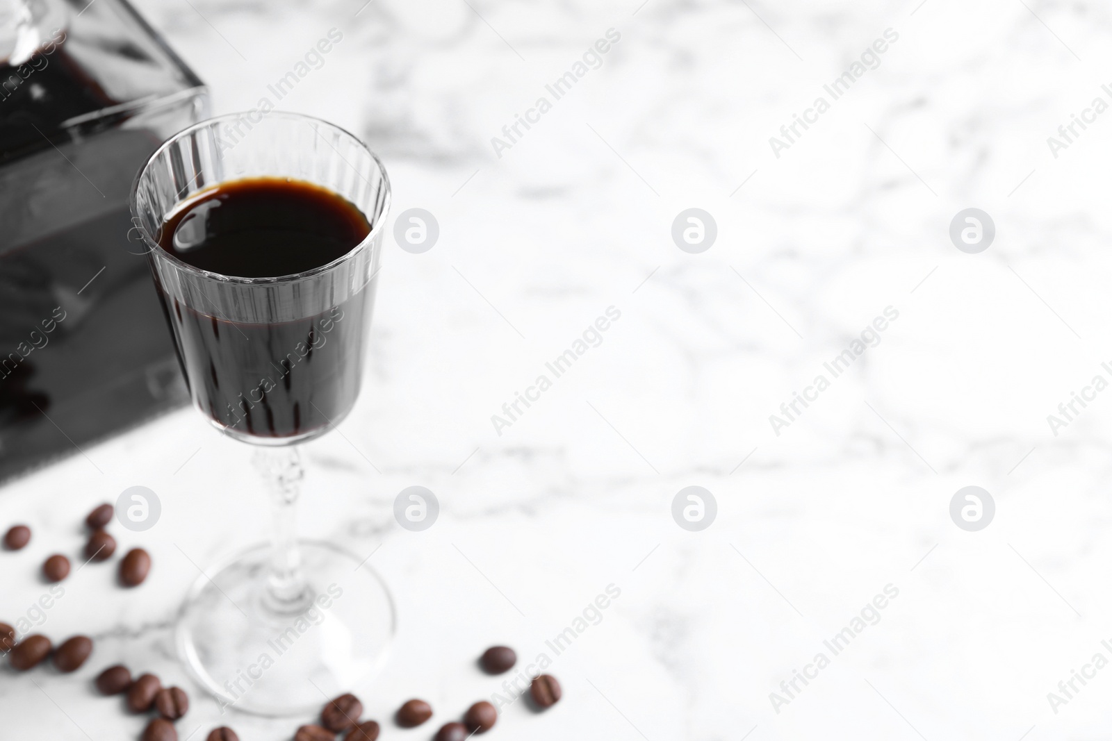 Photo of Coffee liqueur and beans on white marble table. Space for text