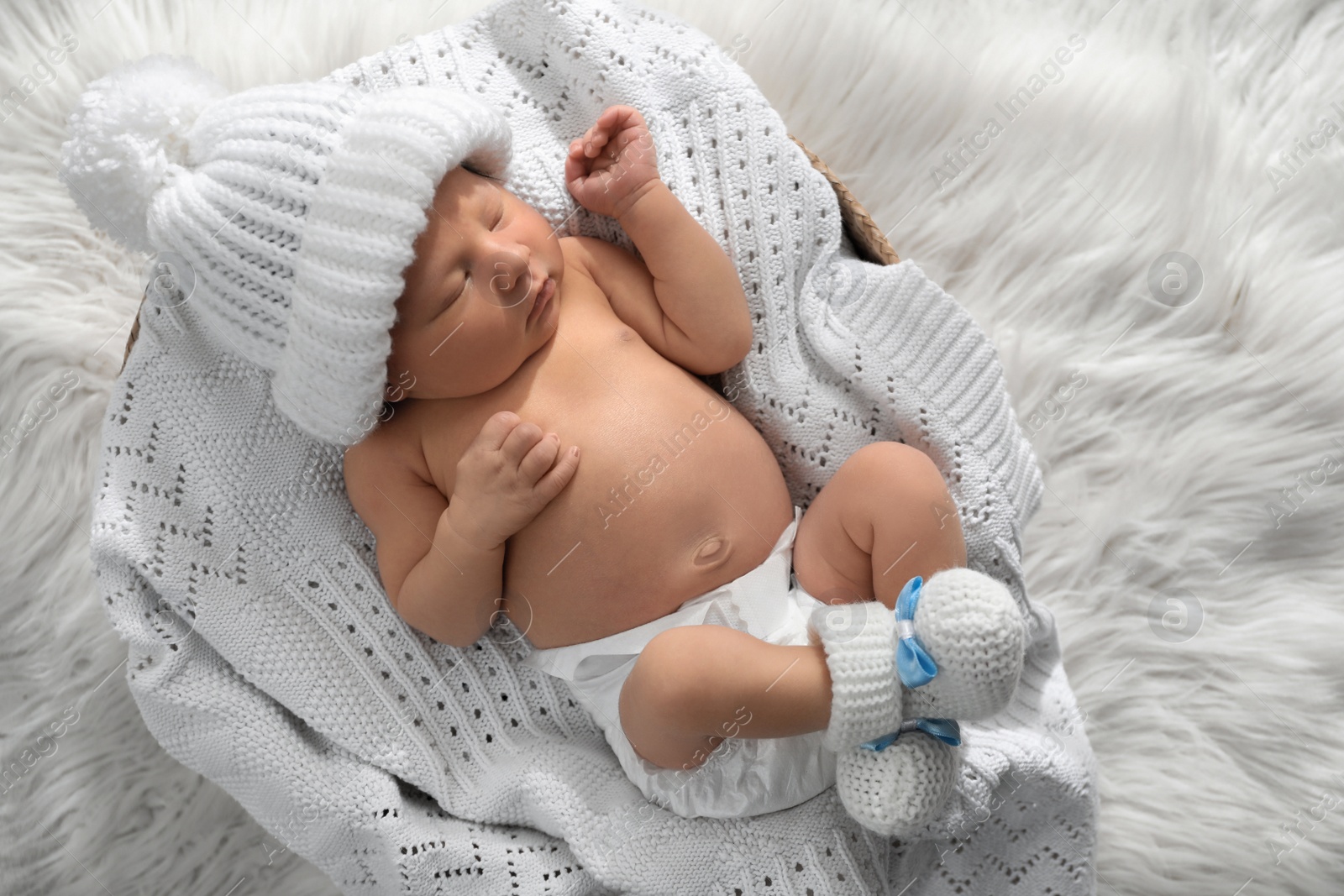 Photo of Cute newborn baby in warm hat and socks sleeping on knitted blanket, top view