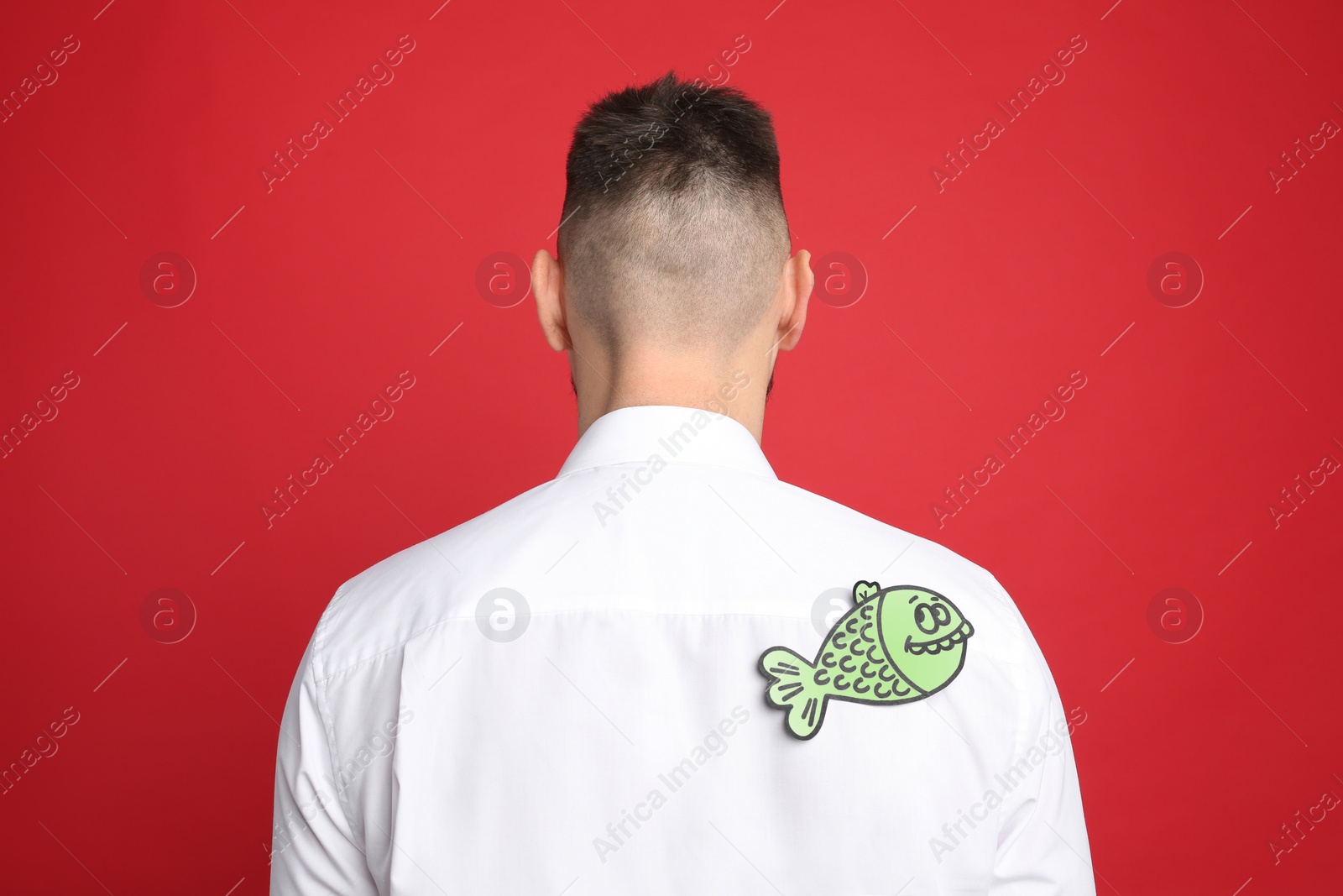 Photo of Man with paper fish on back against red background. April fool's day